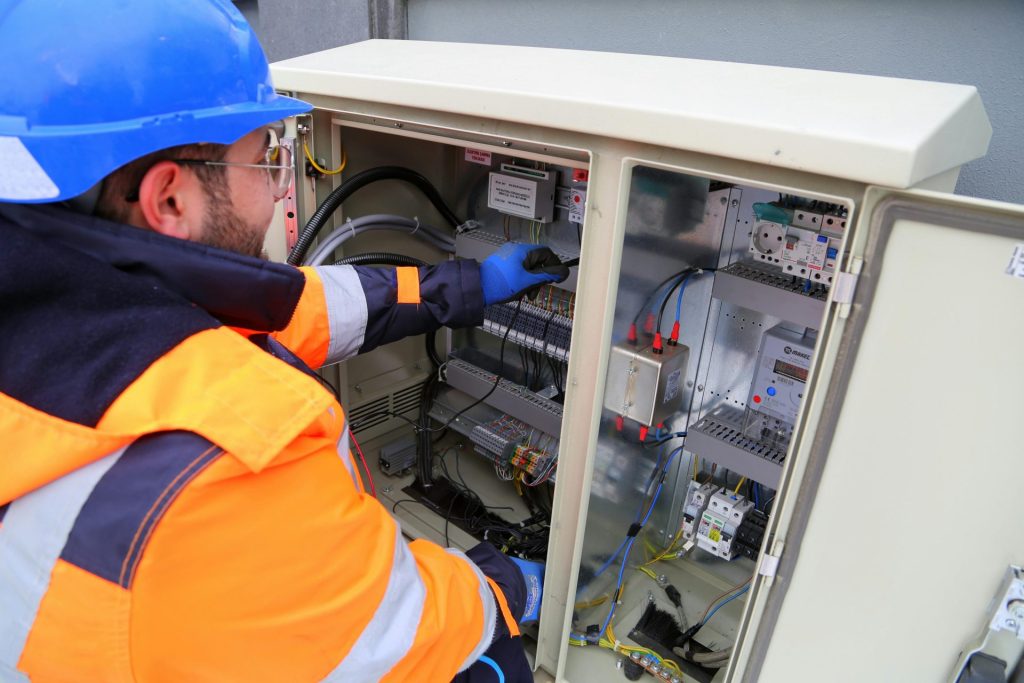 Ein Ingenieur in Schutzausrüstung arbeitet an einem elektrischen Außenverteilerkasten und stellt die Funktionsfähigkeit des Systems sicher.